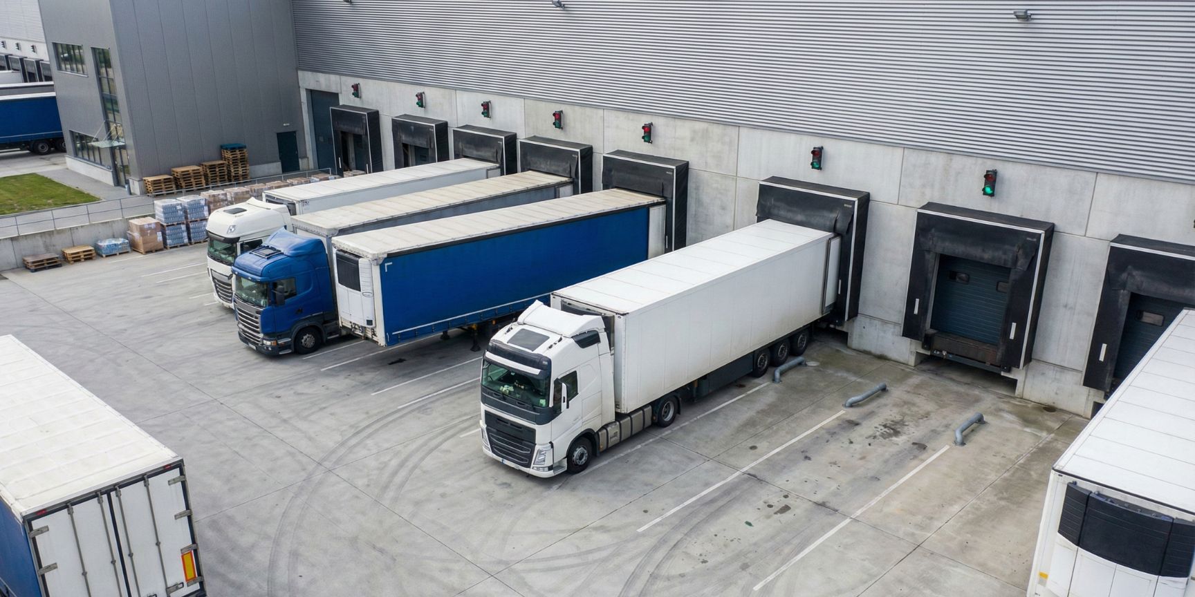 Exterior view of a modern logistics centre with several trucks docked at loading ramps, including dock shelters and a spacious loading yard for rear loading